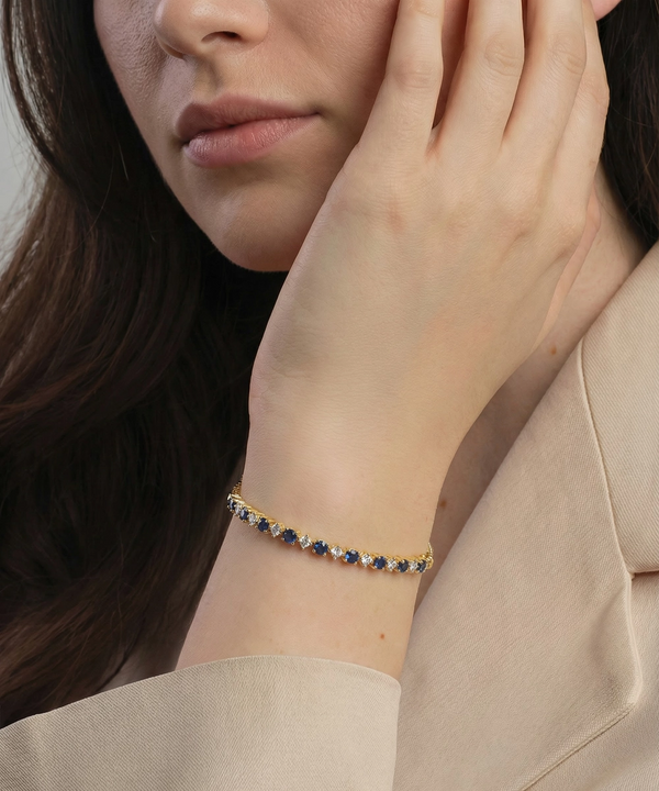 Close-up of a person wearing a gold bracelet with blue stones, touching their face.