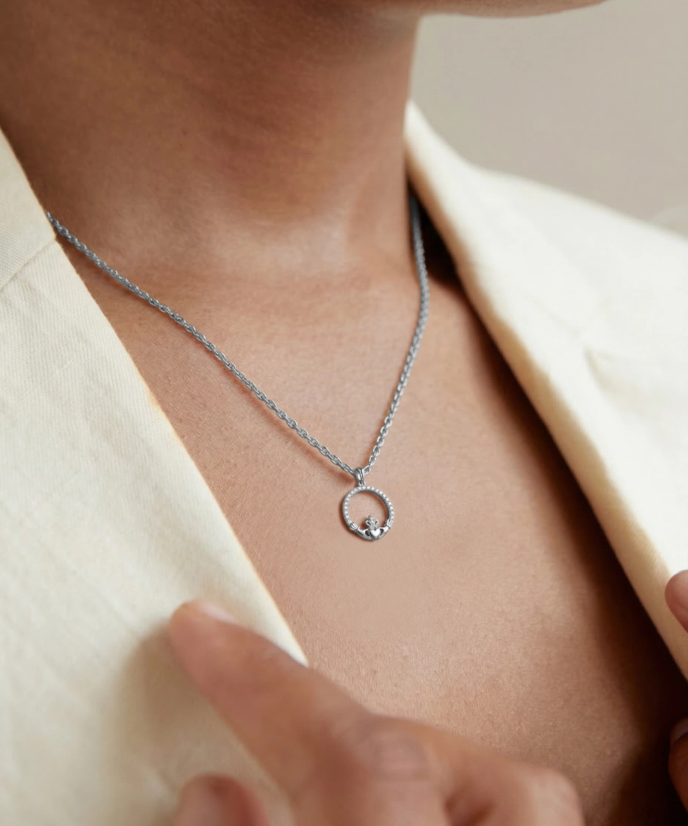Silver necklace with a circular pendant worn by a person in a beige outfit.