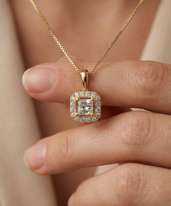 Gold necklace with a diamond pendant held by a hand against a neutral background