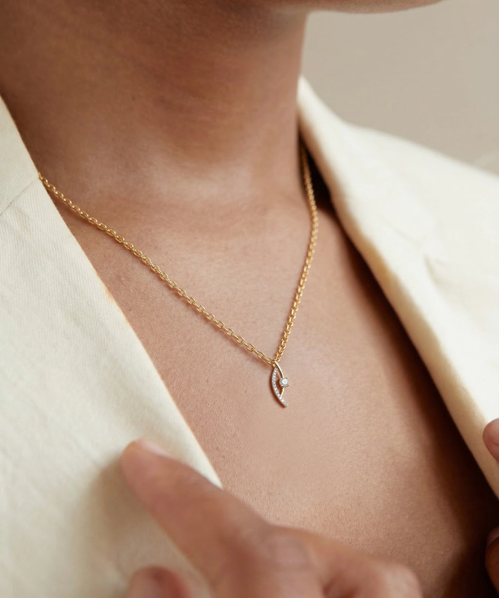 Gold necklace with a delicate pendant worn by a person in a light-colored outfit.
