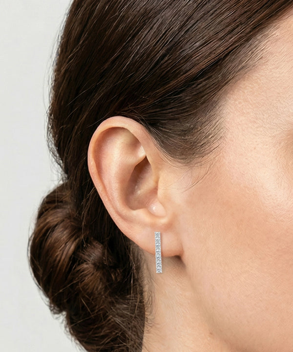Close-up of an ear wearing a silver hoop earring with a plain background