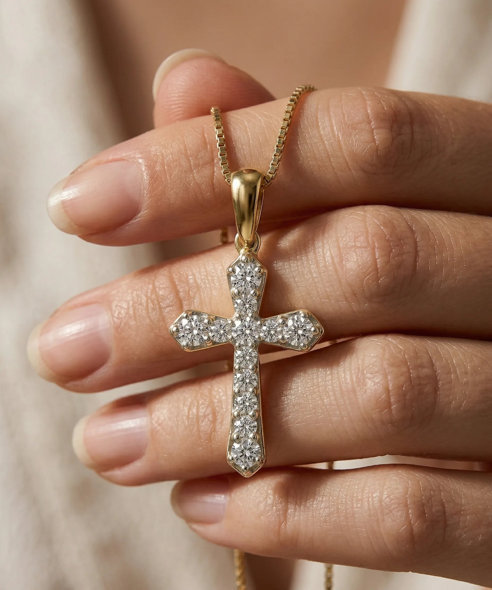 Gold cross necklace with diamonds held between fingers against a neutral background