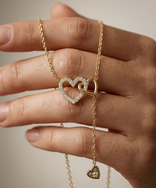 Gold necklace with a heart pendant held by a hand against a neutral background