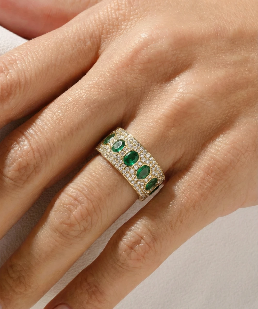 Gold ring with emeralds on a hand against a neutral background