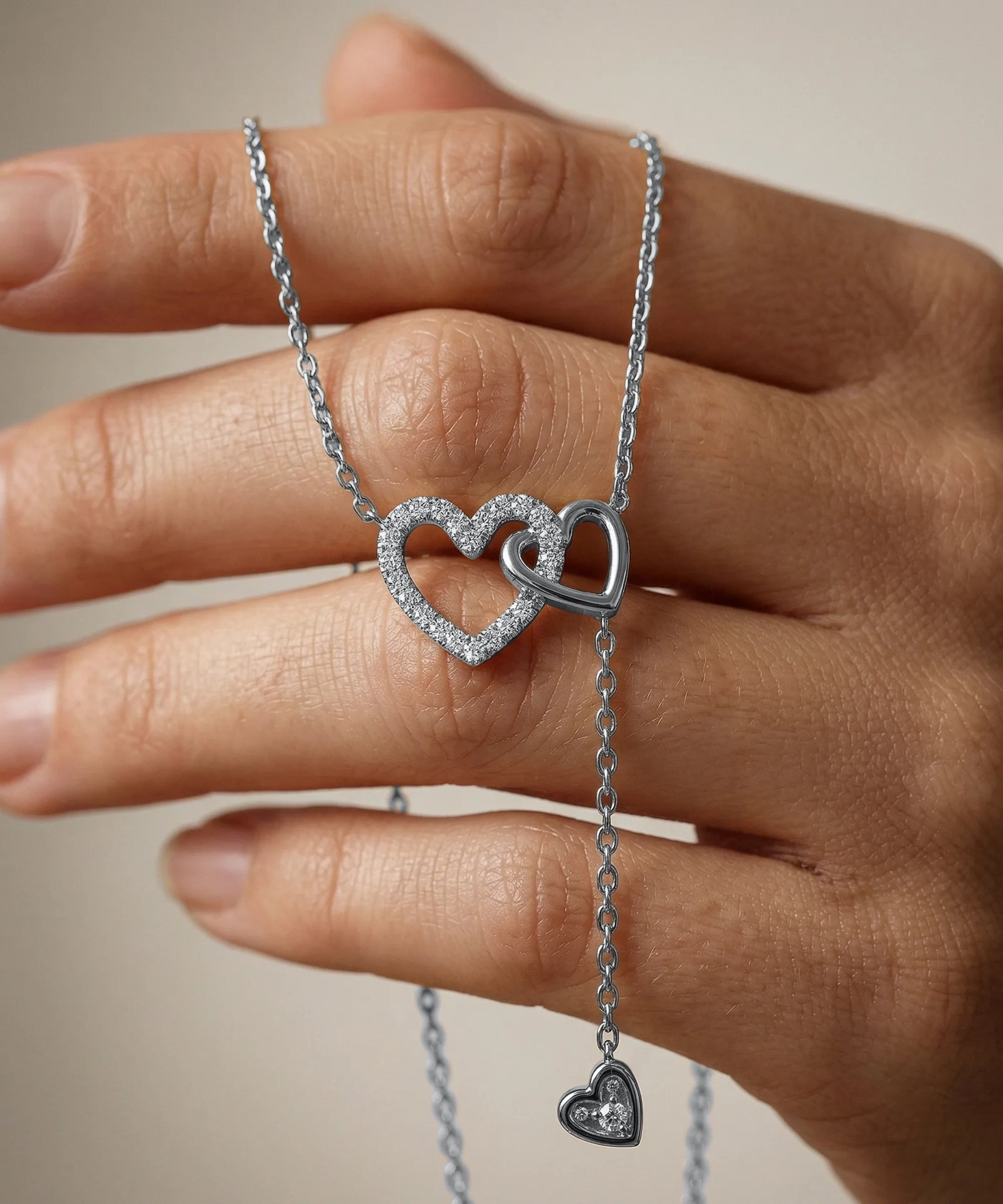 Silver heart-shaped necklace held by a hand against a neutral background