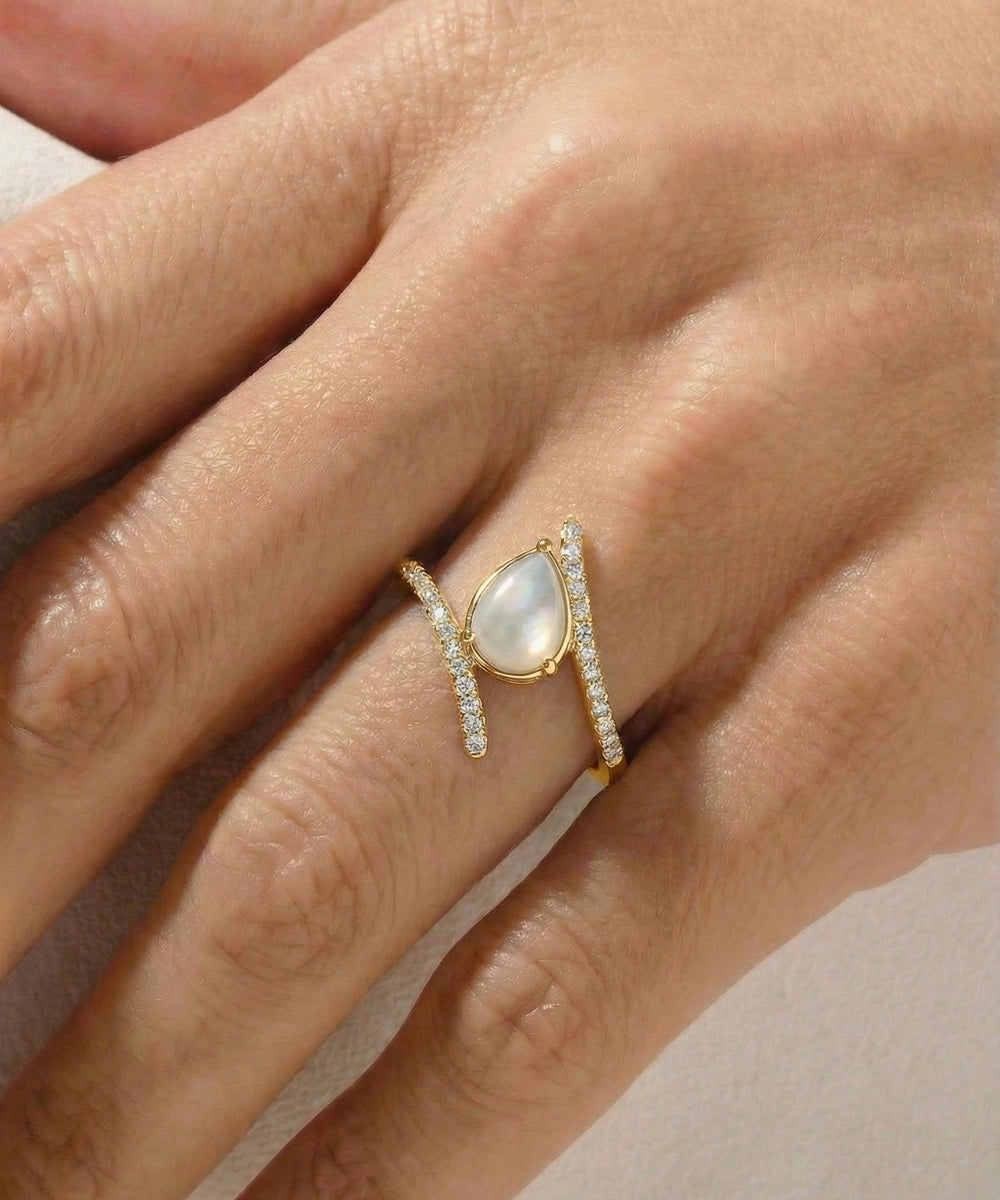 Gold ring with a central gemstone on a hand against a neutral background