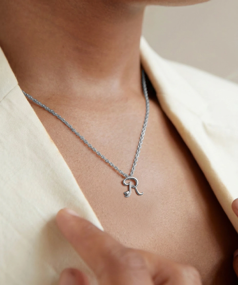 Silver necklace with a letter 'R' pendant on a person wearing a beige blazer.