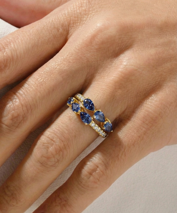 Gold ring with blue gemstones on a hand against a neutral background