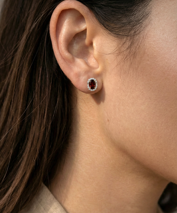 Close-up of an ear wearing a silver earring with a red gemstone.