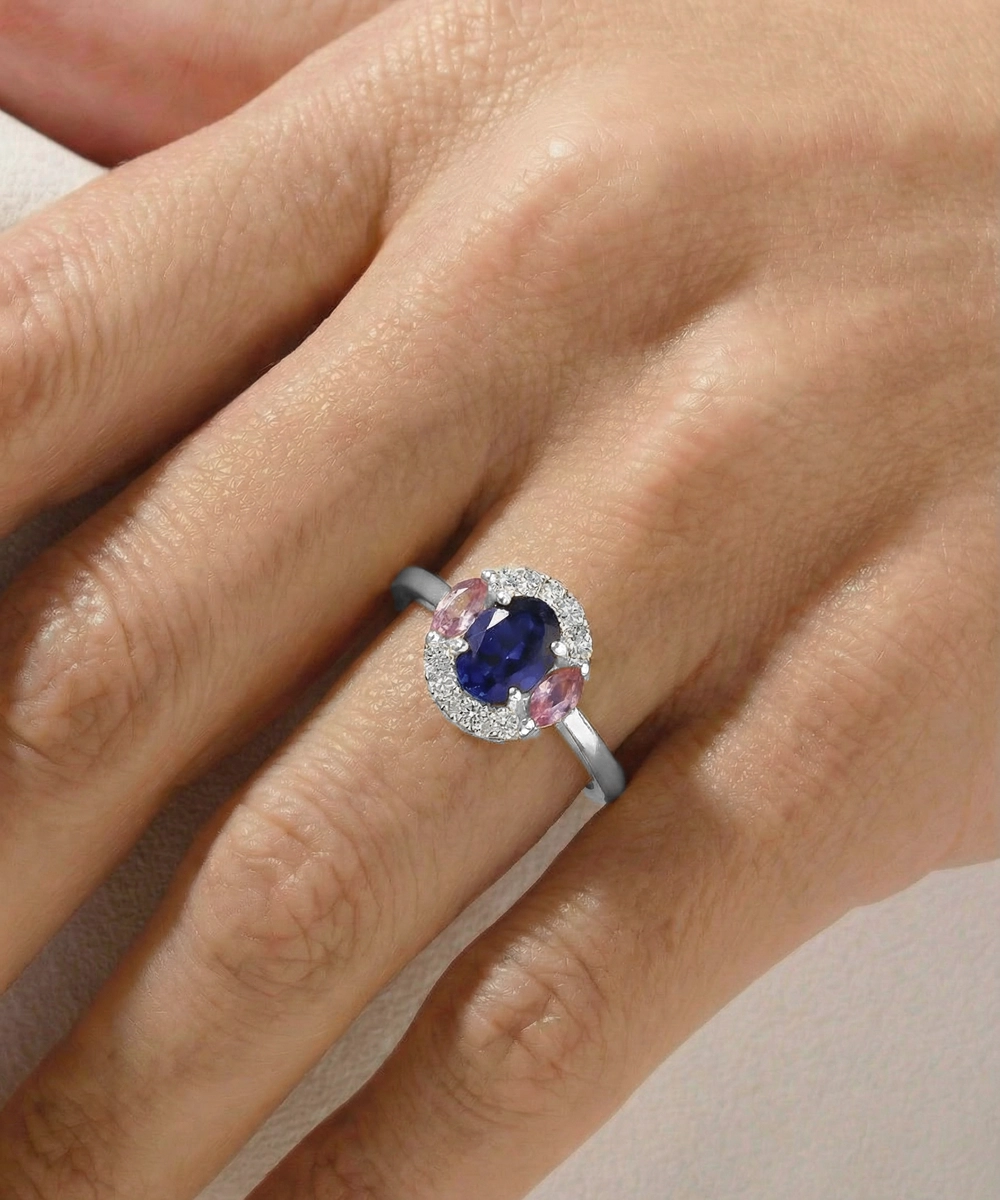 Ring with a blue gemstone and pink accents on a hand against a neutral background