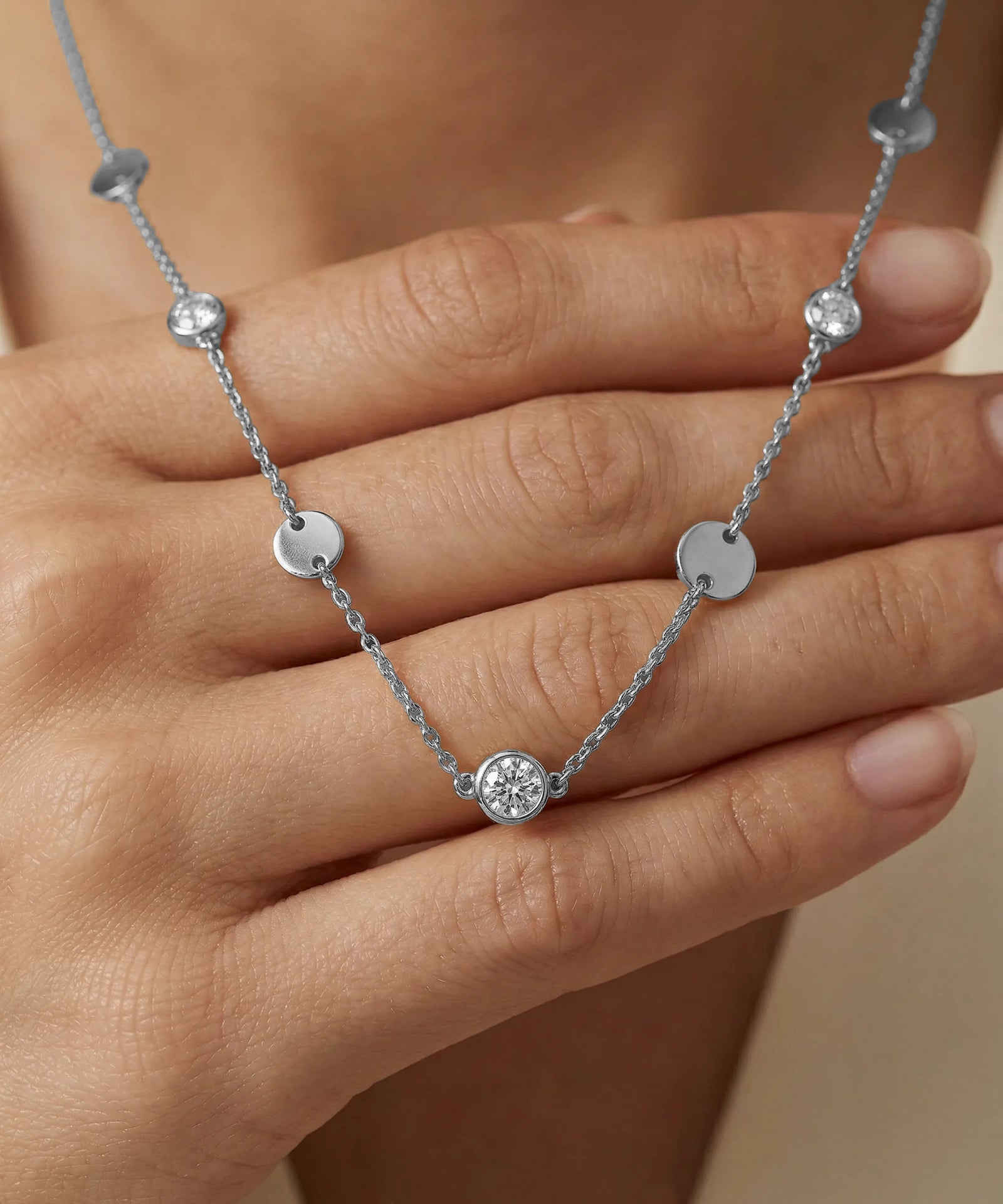Silver necklace with small round pendants held by a hand against a neutral background