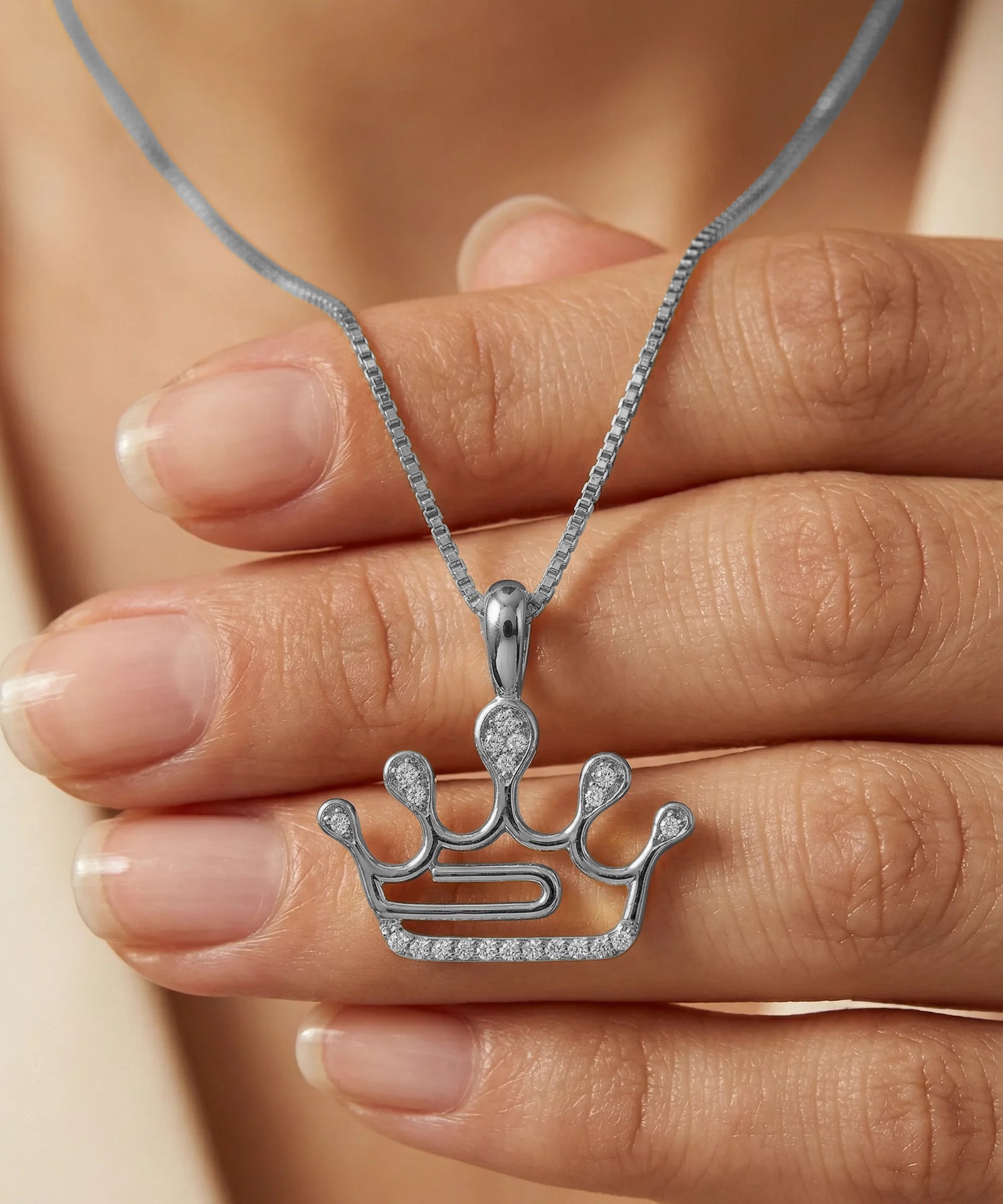 Silver crown-shaped pendant on a chain held between fingers