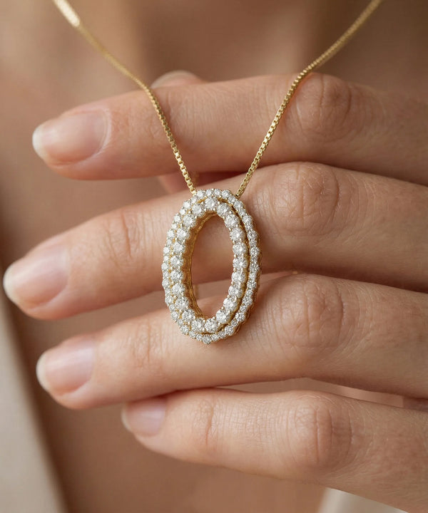 Gold necklace with a pearl pendant held by a hand against a neutral background