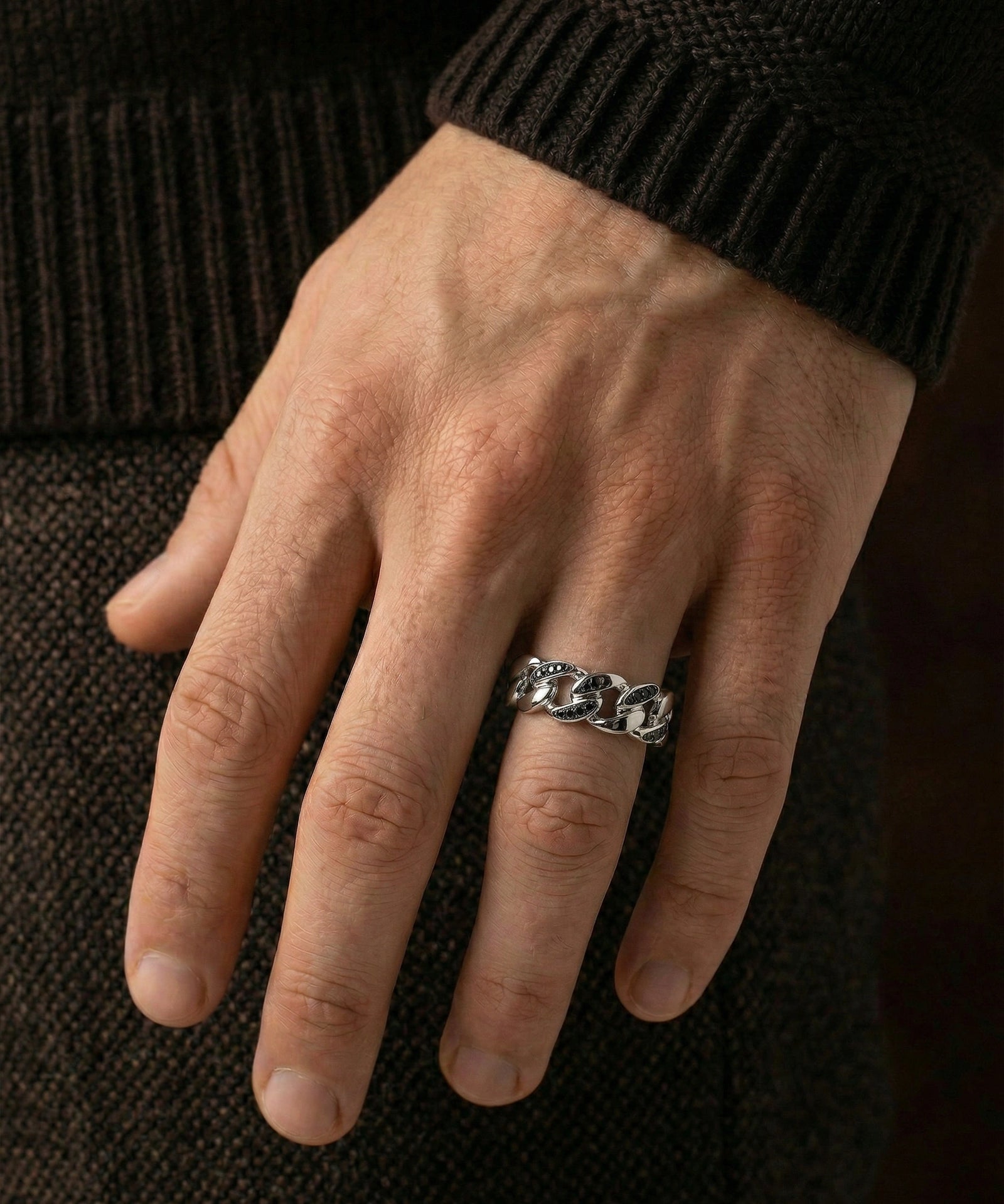 Hand wearing a silver chain ring on a dark background