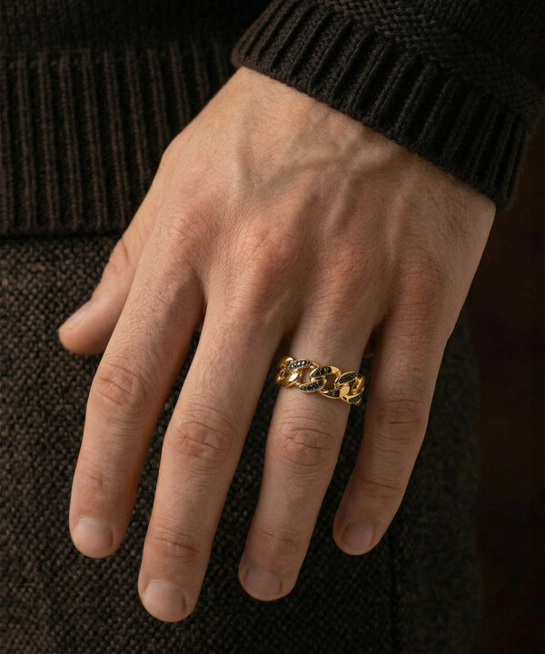 Hand wearing a gold chain ring on a dark textured background