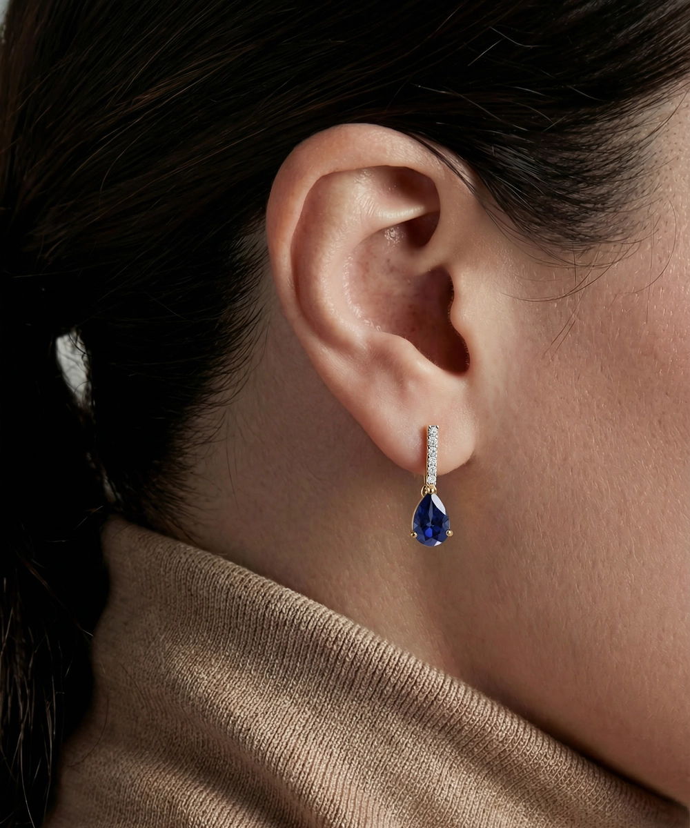 Close-up of a person wearing a blue teardrop earring with a blurred background