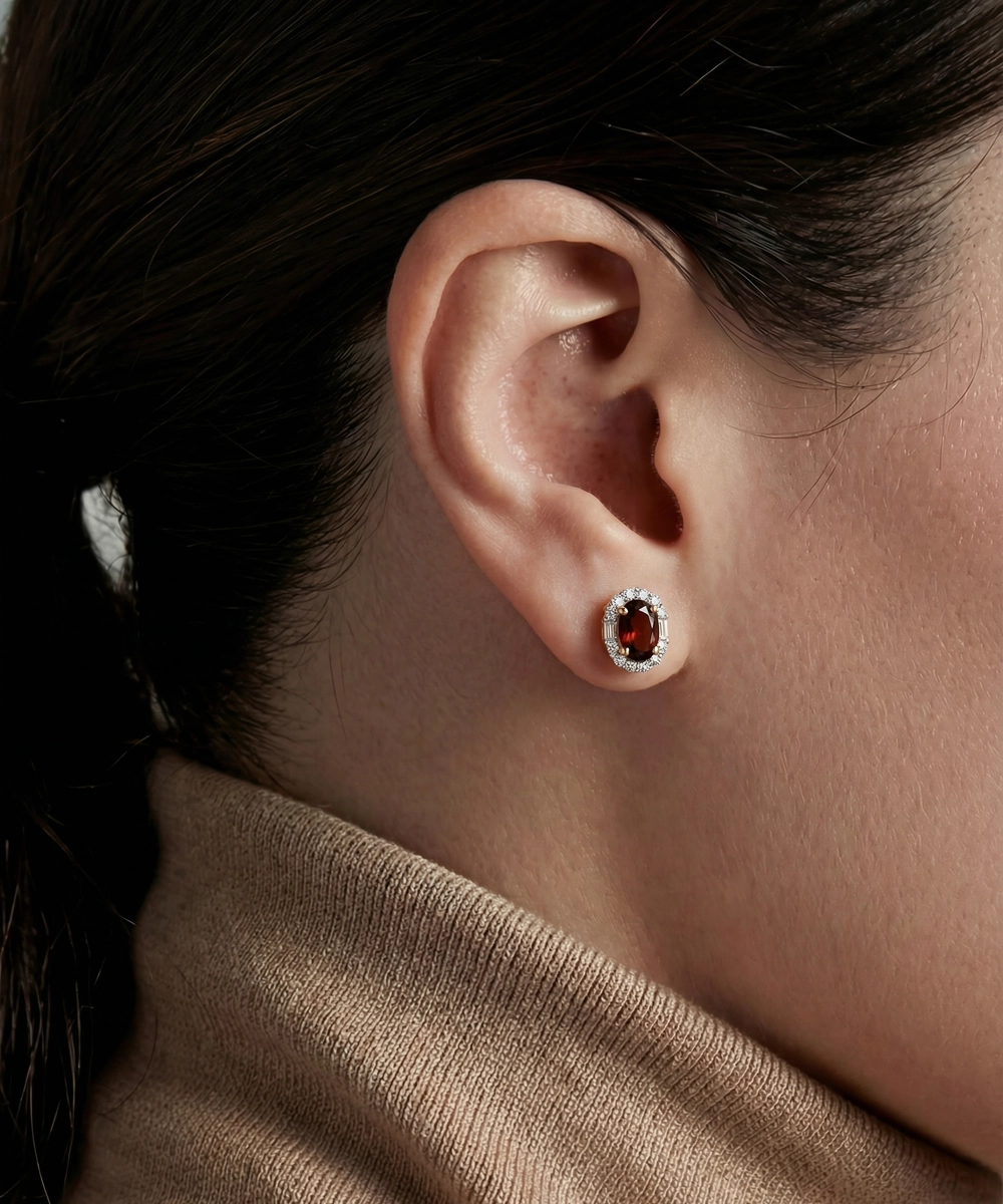 Close-up of an ear wearing a round earring with a dark gemstone, against a blurred background.