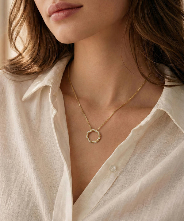 Close-up of a person wearing a gold necklace with a circular pendant, set against a neutral background.
