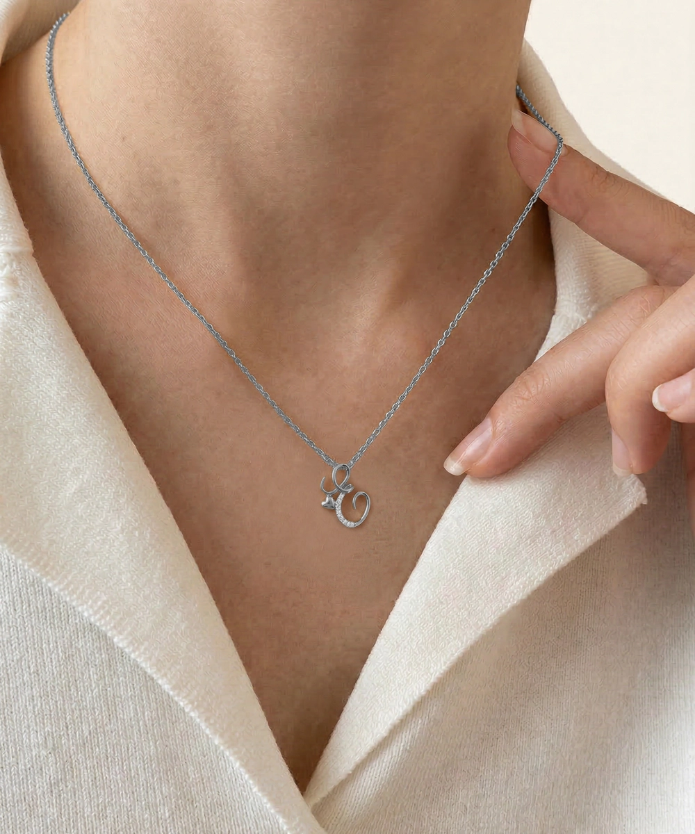 Silver necklace with a letter 'R' pendant worn by a person in a light-colored garment.