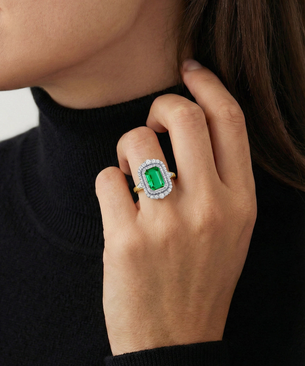 Close-up of a hand wearing an emerald ring with a black background