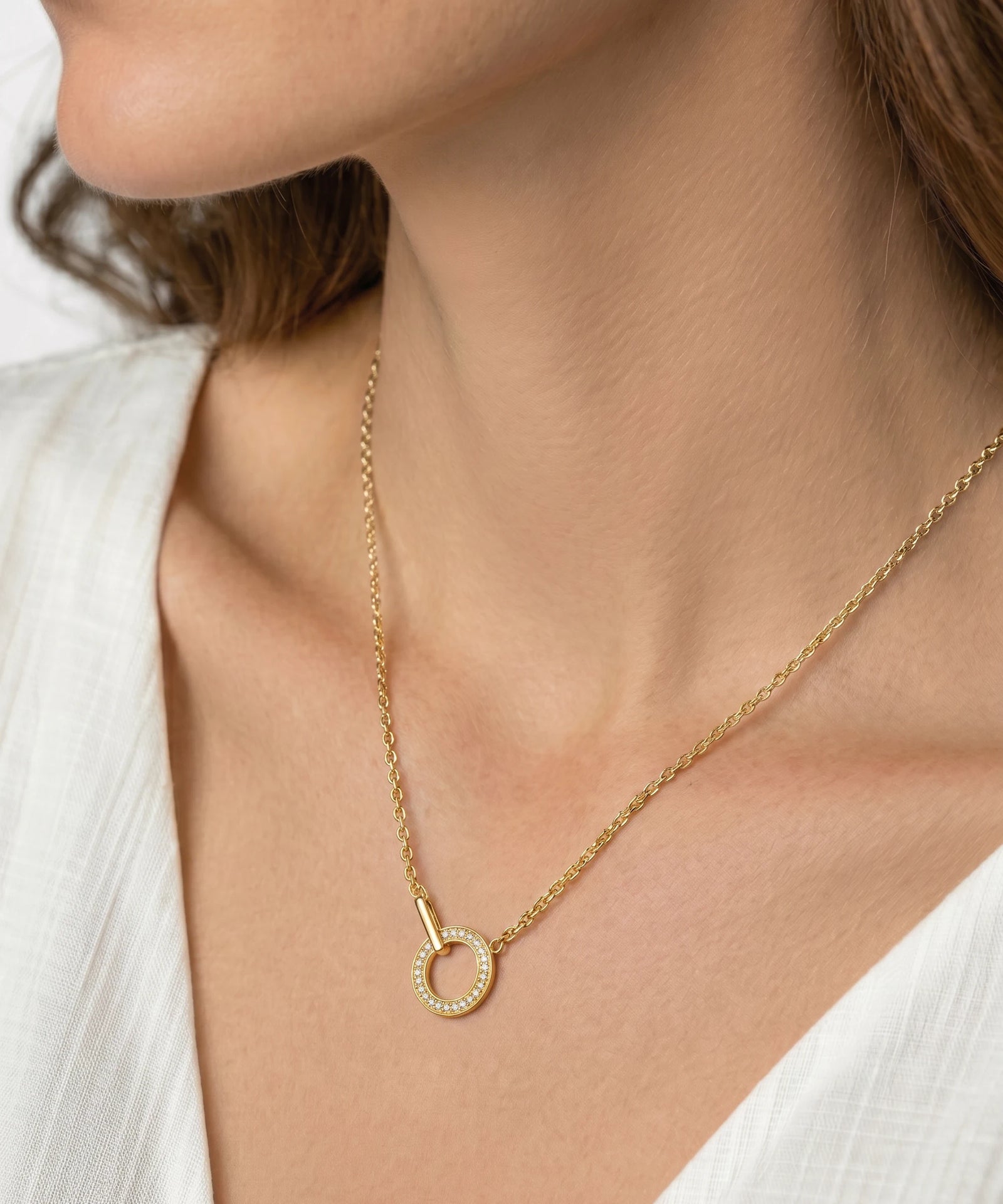 Gold necklace with a small circular pendant worn by a person in a white outfit.