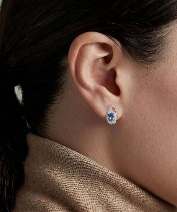 Close-up of an ear wearing a blue gemstone earring with a blurred background
