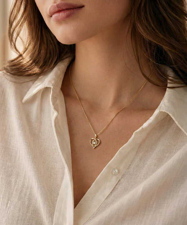 Close-up of a person wearing a gold necklace with a heart pendant, set against a neutral background.