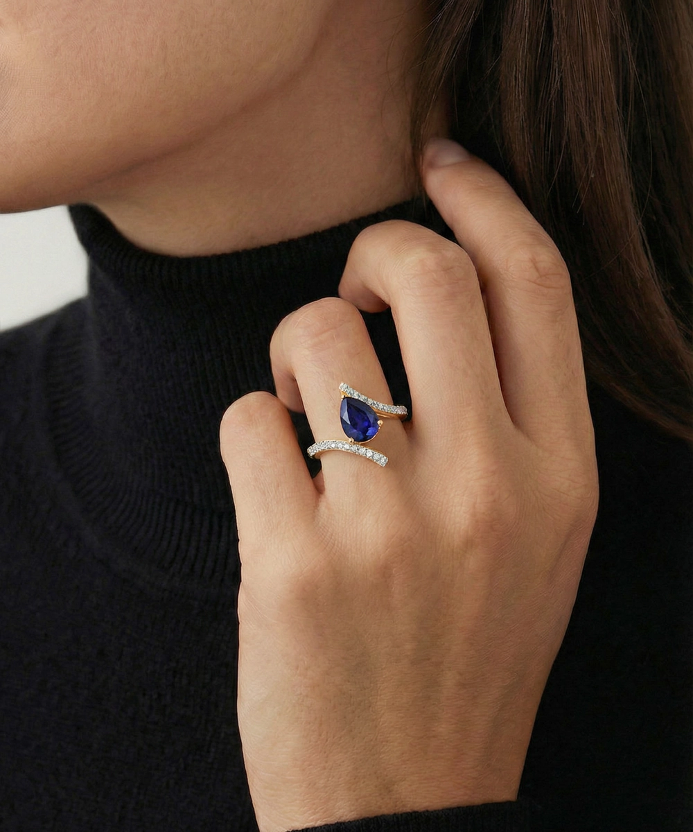 Close-up of a hand wearing a ring with a blue gemstone, against a neutral background.