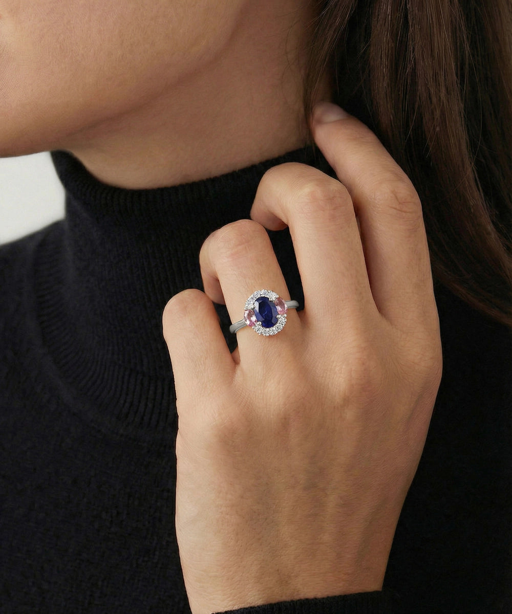 Close-up of a hand wearing a ring with a blue gemstone, against a neutral background.