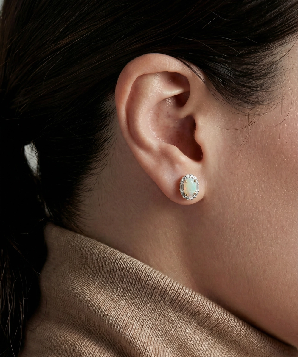 Close-up of an ear wearing a small round earring with a light-colored gemstone, against a neutral background.