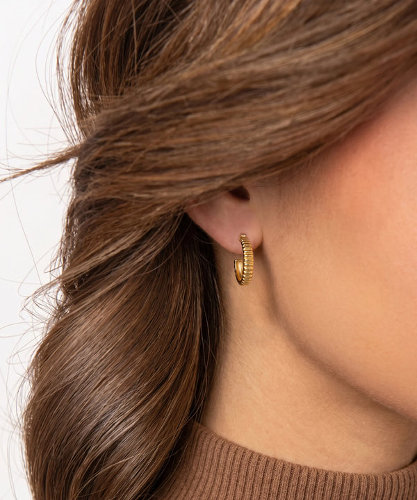 Close-up of a person wearing a gold hoop earring with a neutral background
