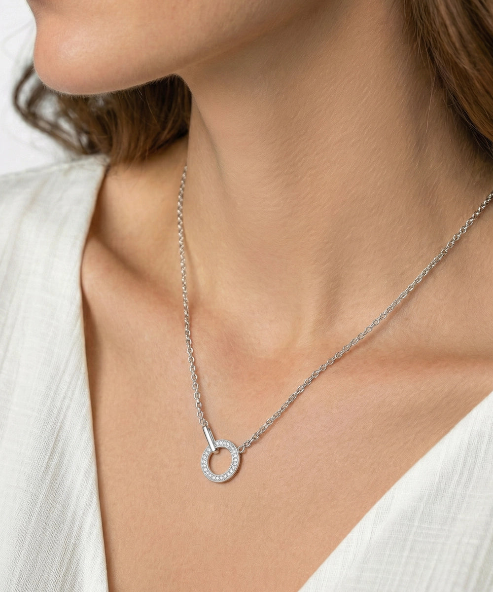 Silver necklace with a circular pendant worn by a person in a white outfit.