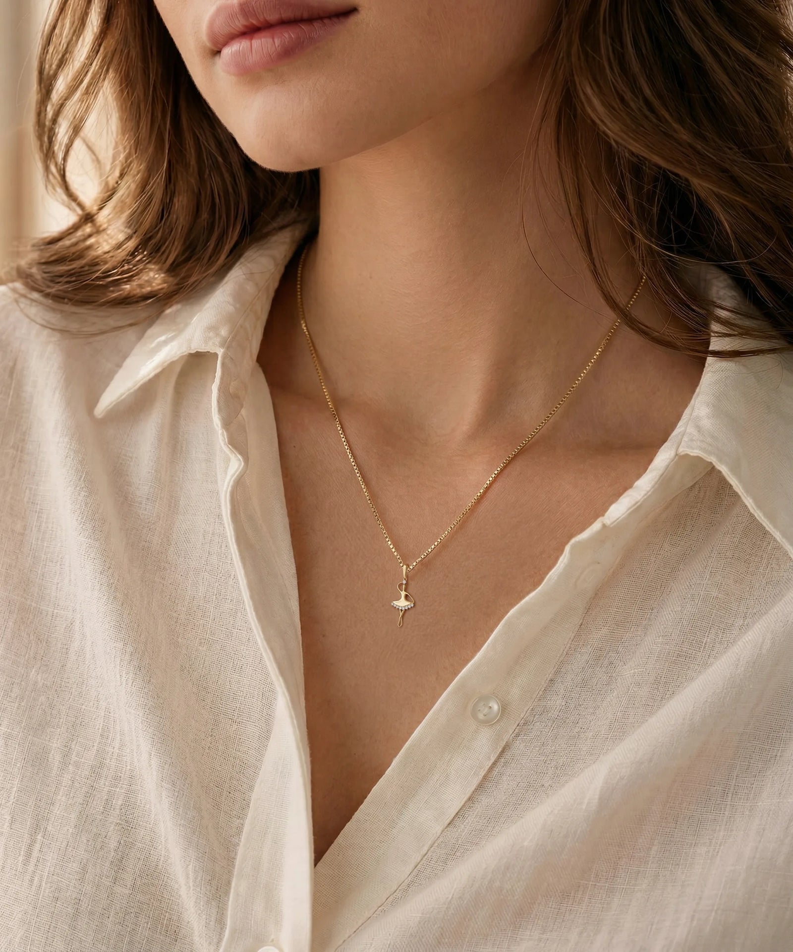Close-up of a person wearing a delicate gold necklace with an oval pendant against a neutral background.