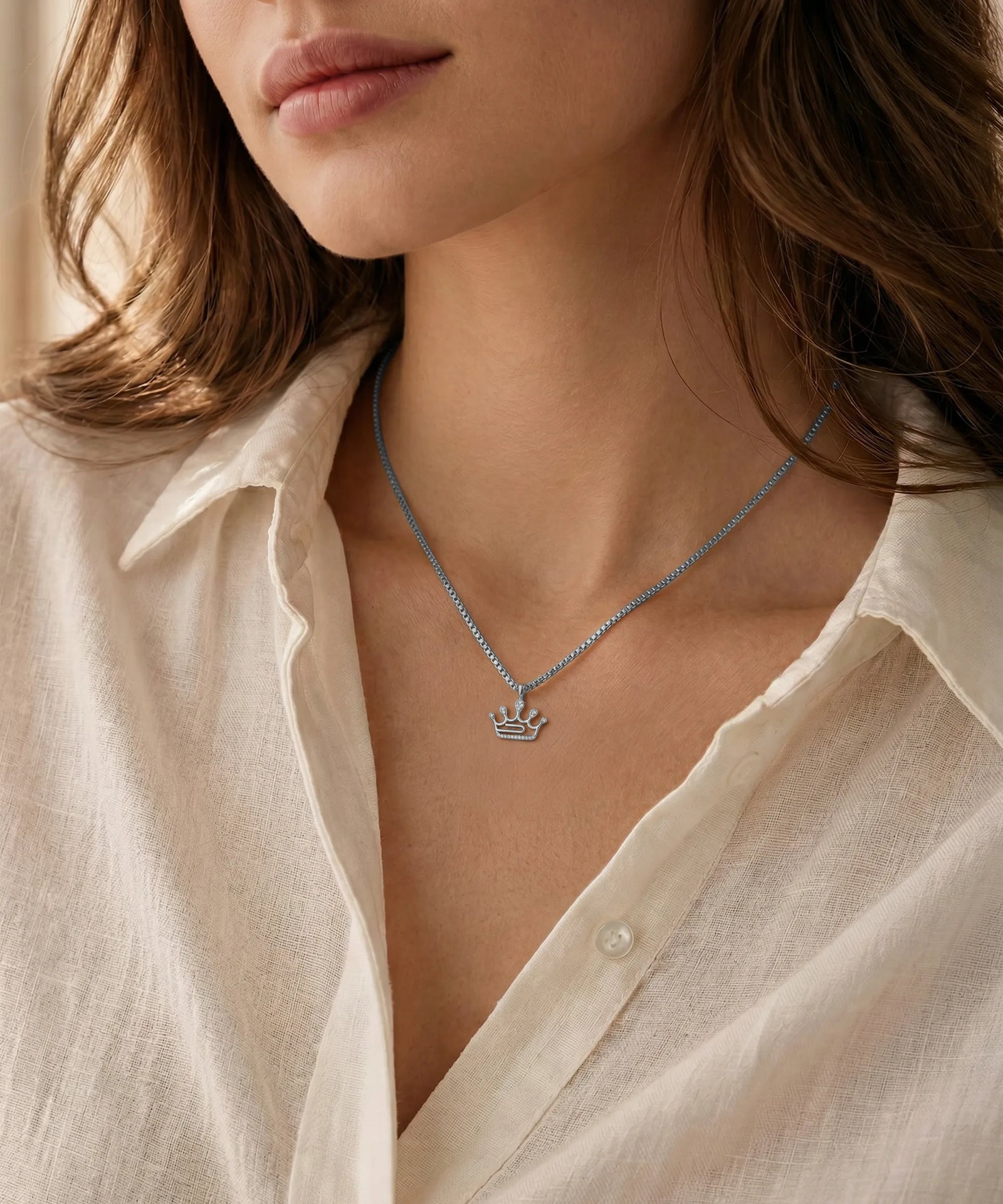 Necklace with a crown pendant worn by a person in a light-colored shirt.