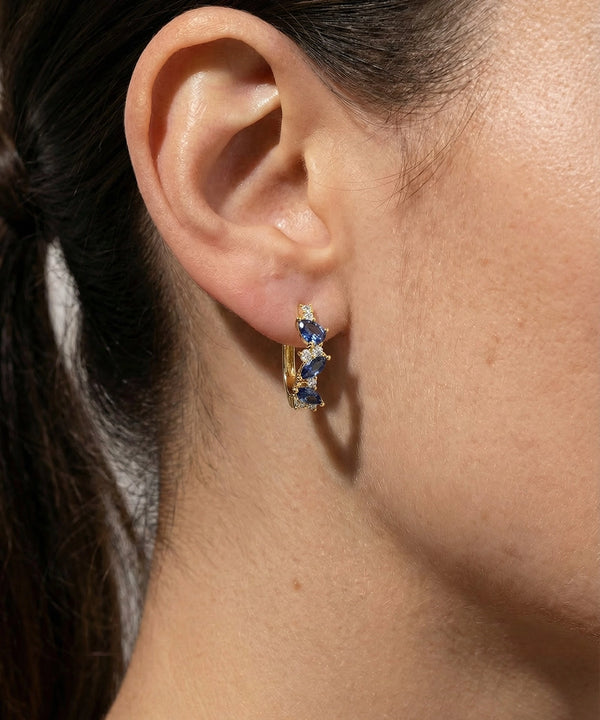 Close-up of an ear wearing a gold earring with blue gemstones.