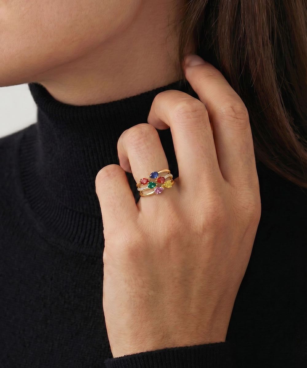 Close-up of a hand wearing a colorful gemstone ring against a neutral background