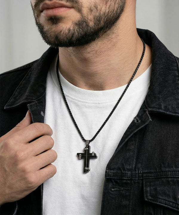 Man wearing a black cross necklace with a white shirt and dark jacket.