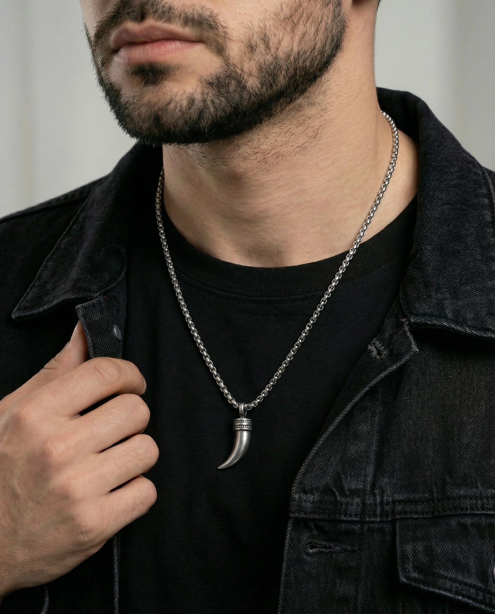 Man wearing a black shirt and dark jacket with a silver necklace featuring a unique pendant.