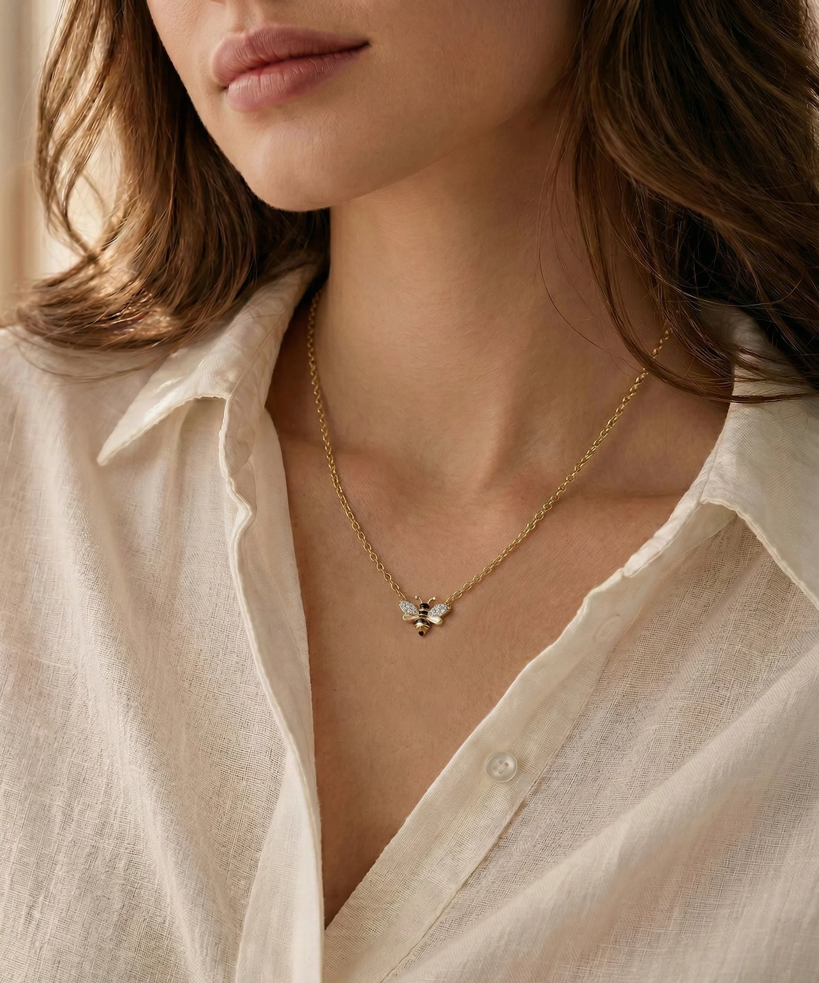 Close-up of a person wearing a gold necklace with a butterfly pendant, against a neutral background.