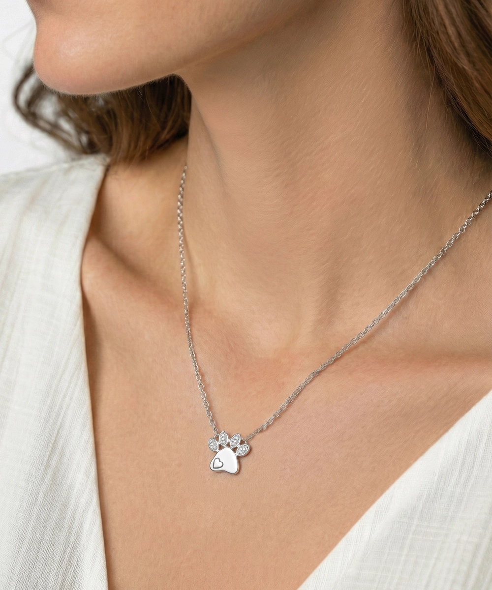 Silver necklace with a paw-shaped pendant worn by a person in a white top.