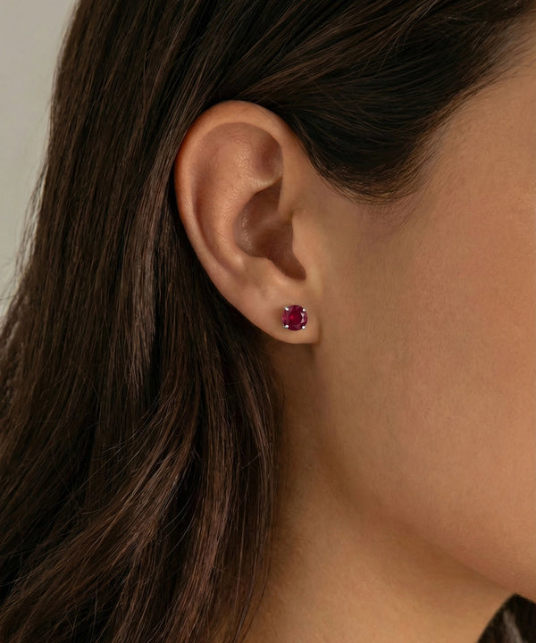 Close-up of an ear wearing a red gemstone earring with blurred background
