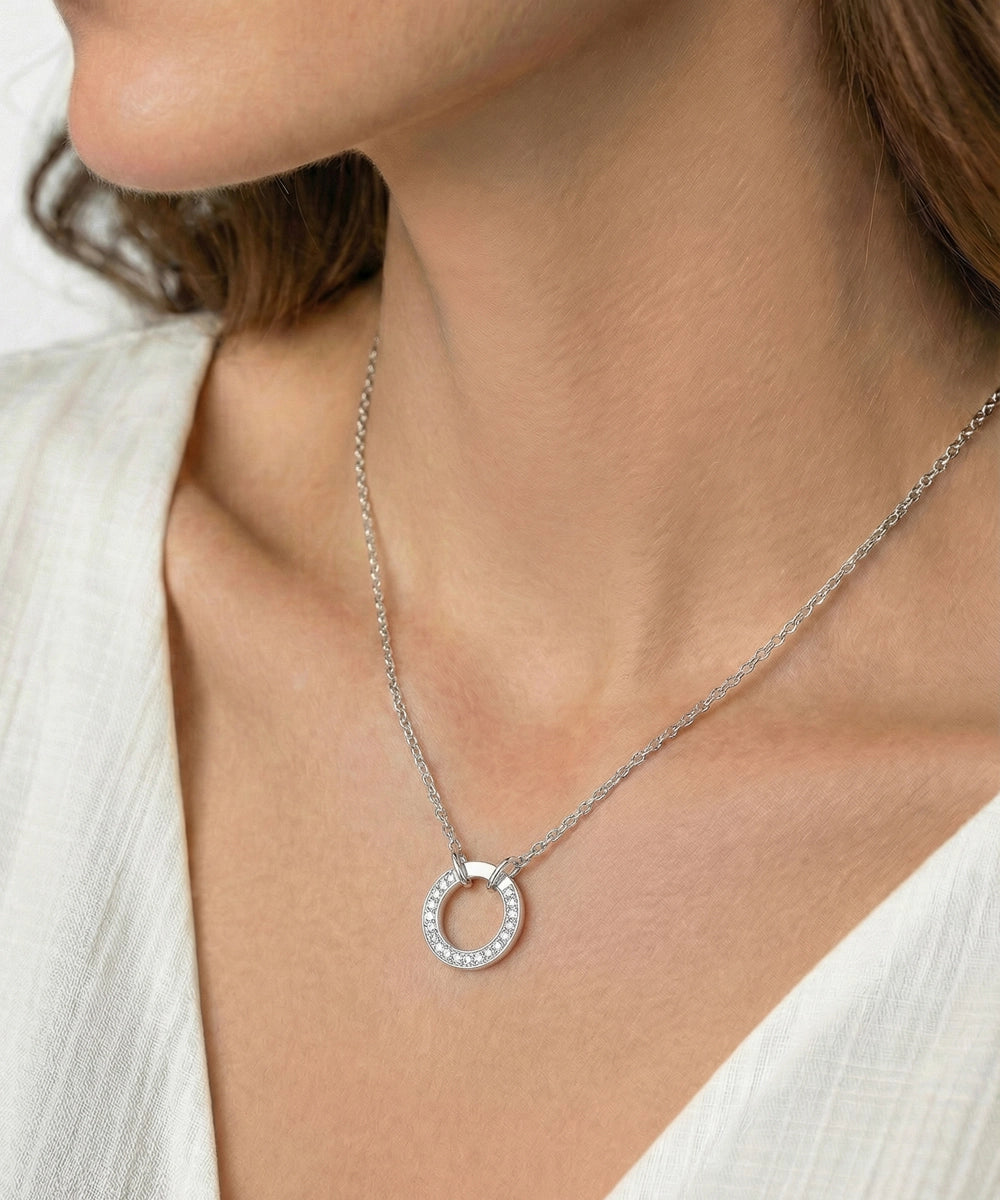 Silver necklace with a circular pendant on a person wearing a white top.