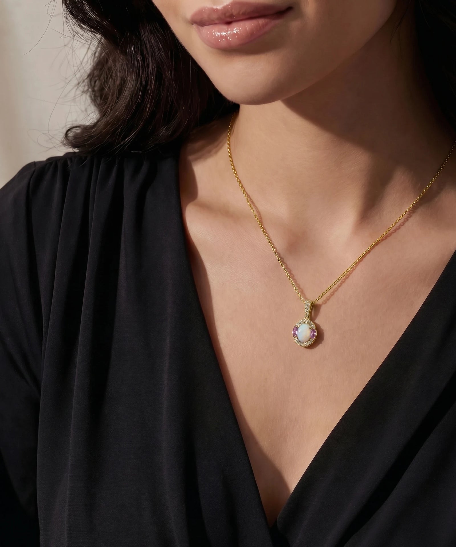 Gold necklace with a green gemstone pendant worn by a person in a black top.