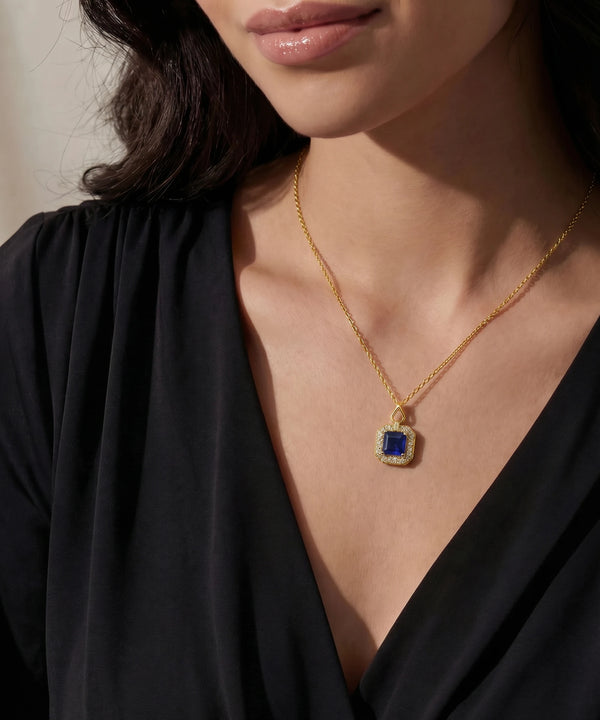 Gold necklace with a blue gemstone pendant worn by a person in a black top.