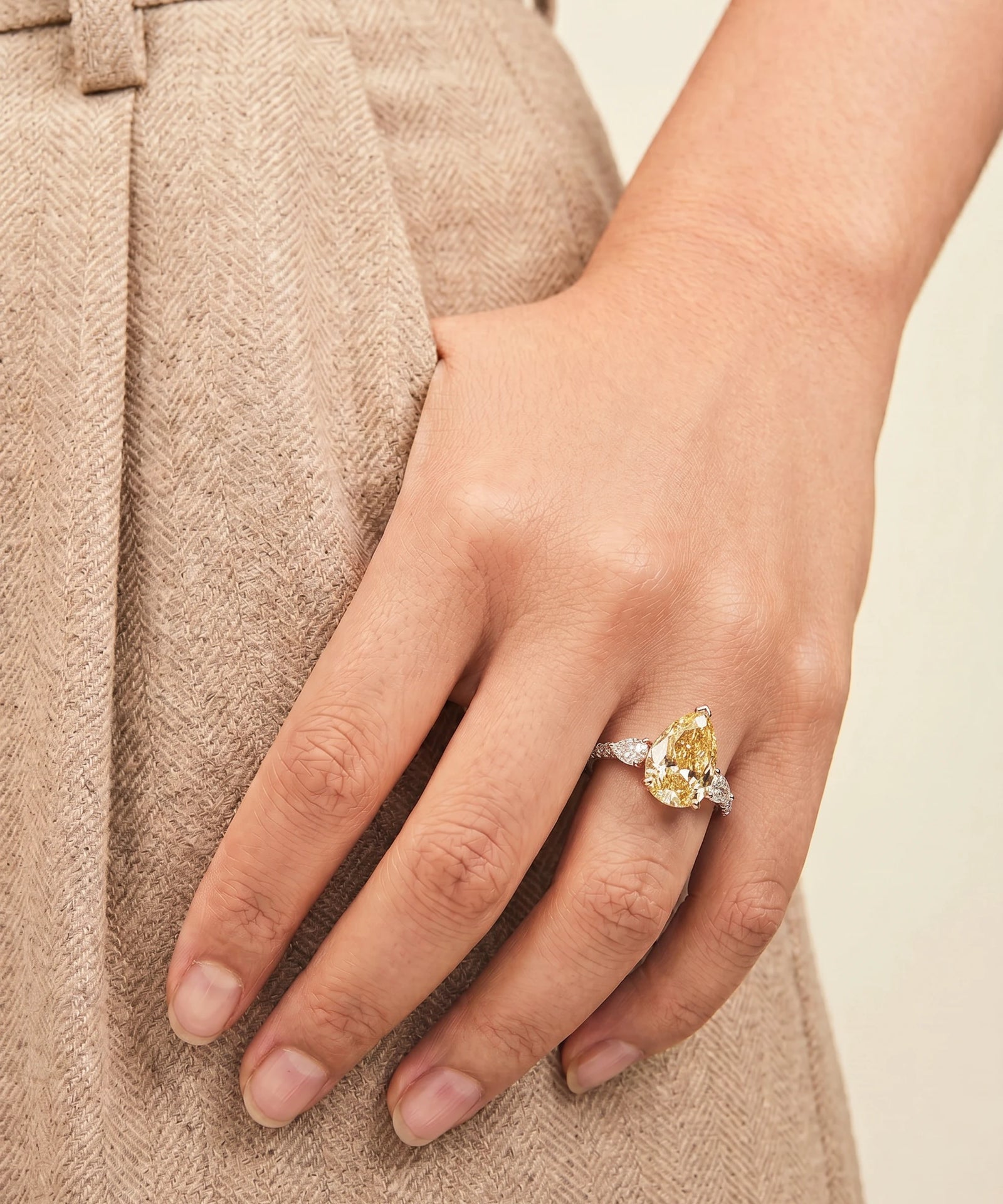 Hand wearing a yellow diamond ring on a neutral background