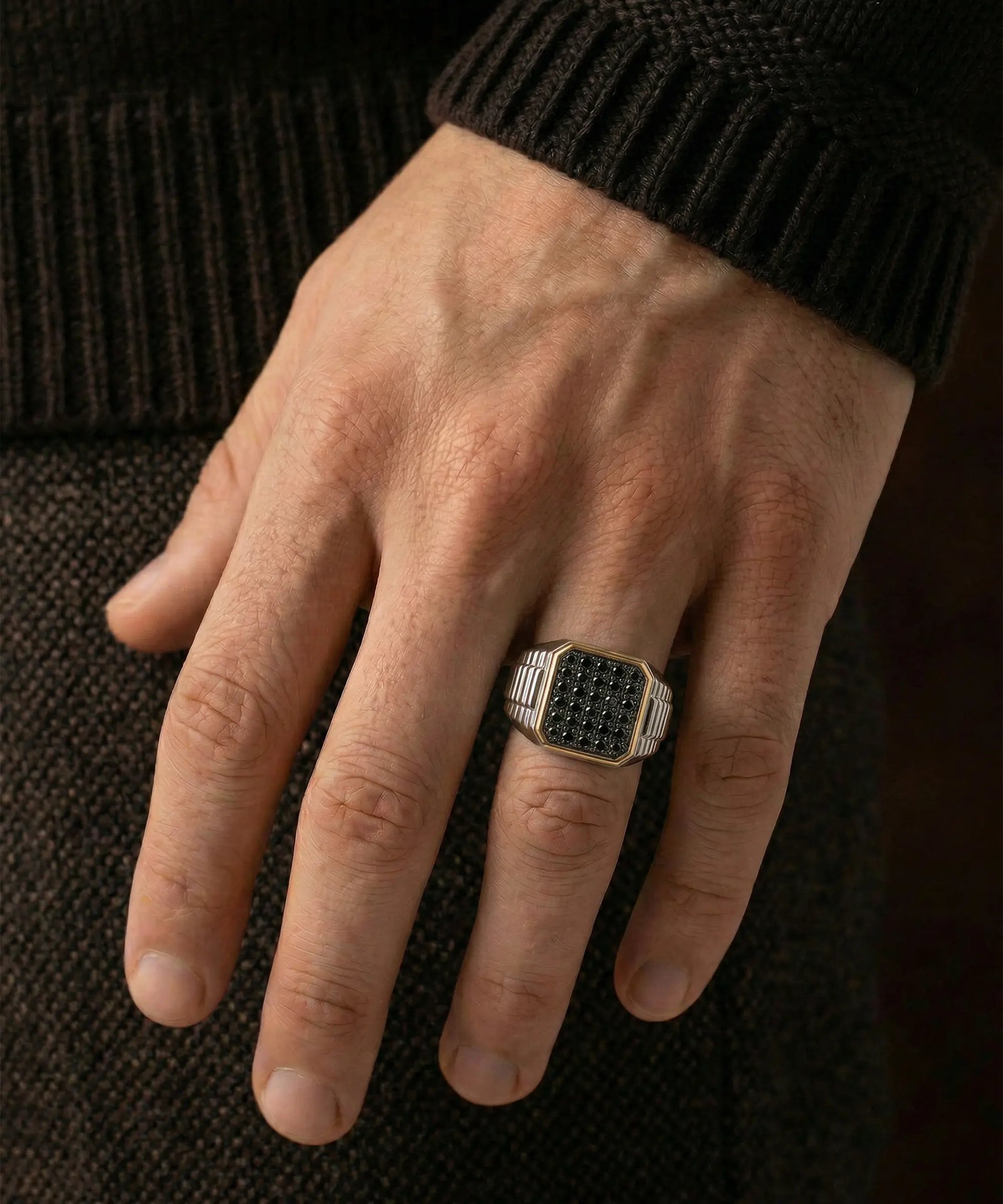Hand wearing a black diamond ring on a dark textured background