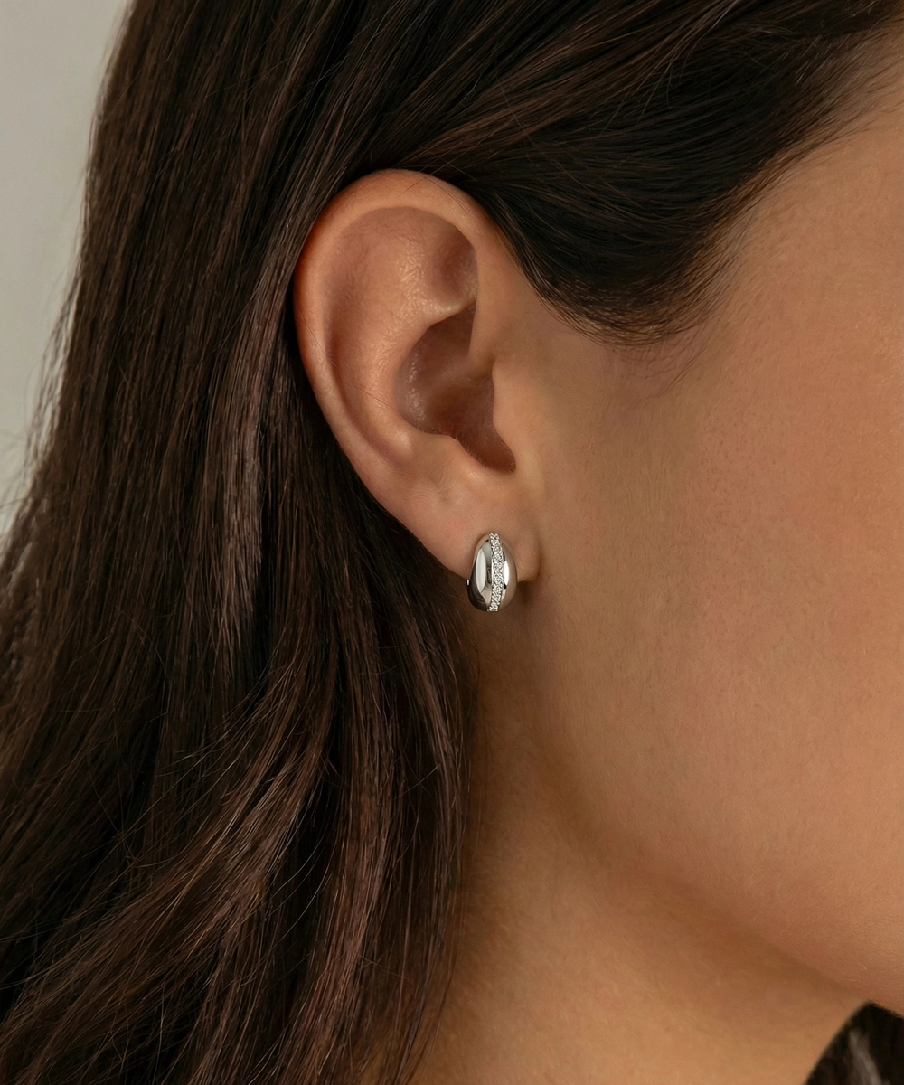 Close-up of an ear wearing a diamond earring with dark hair and skin.
