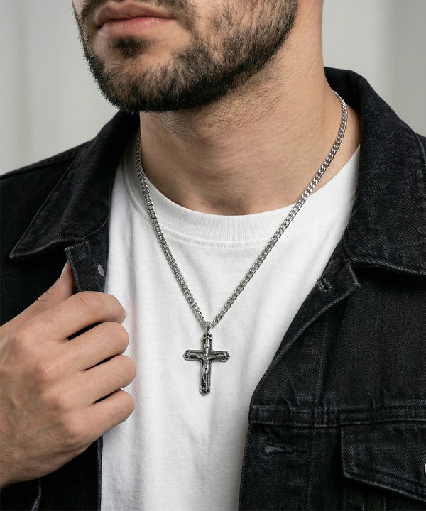Man wearing a black jacket and white shirt with a silver cross necklace.