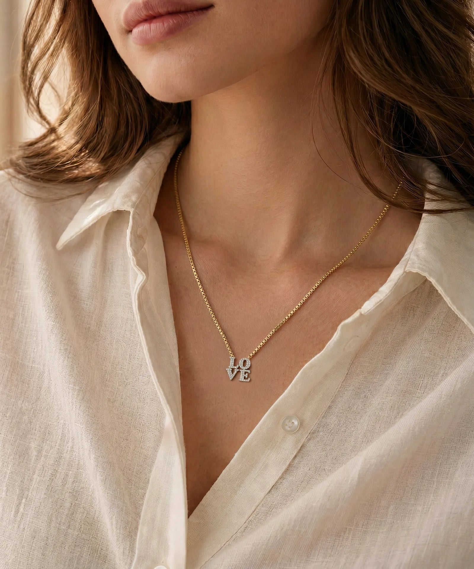 Close-up of a person wearing a delicate gold necklace with an oval pendant against a neutral background.