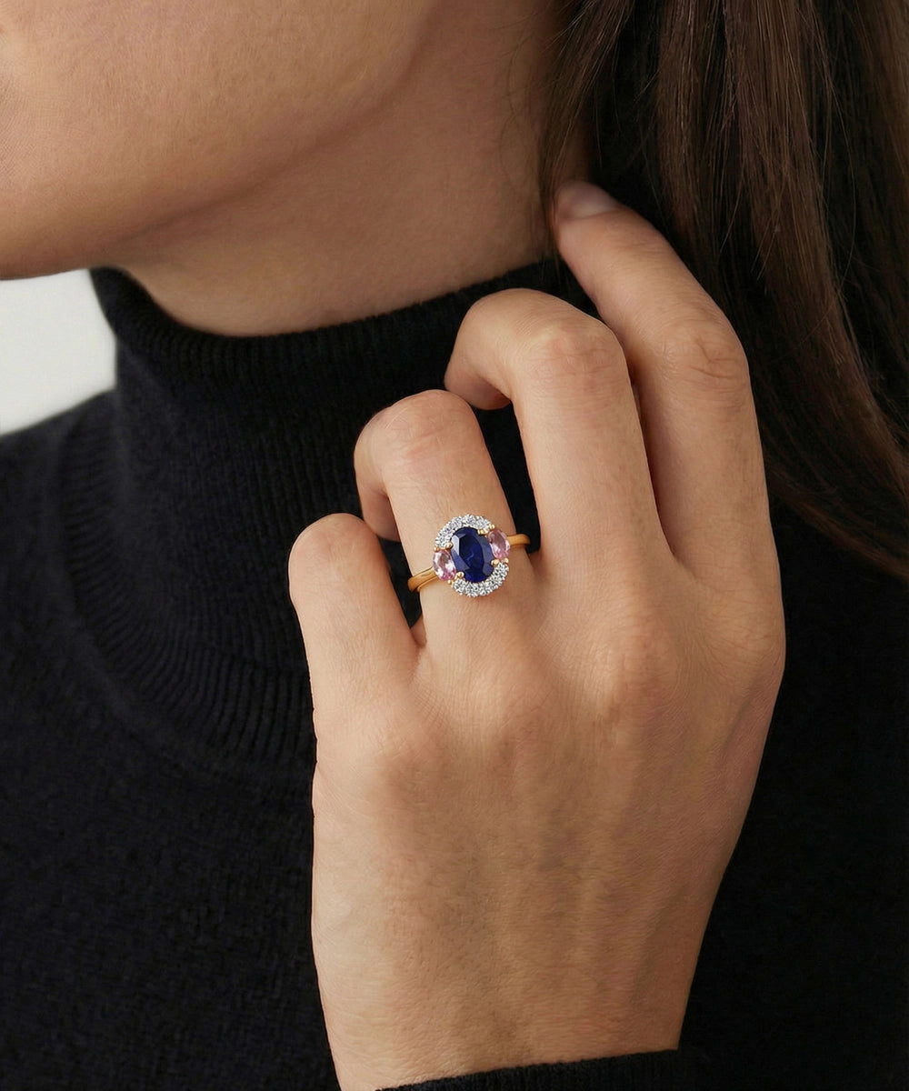 Close-up of a hand wearing a ring with a blue gemstone, against a neutral background.
